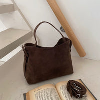 Sac cabas daim compact femme marron posé près d’un livre ouvert
