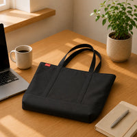 Sac cabas oxford grand format noir posé sur un bureau avec ordinateur portable